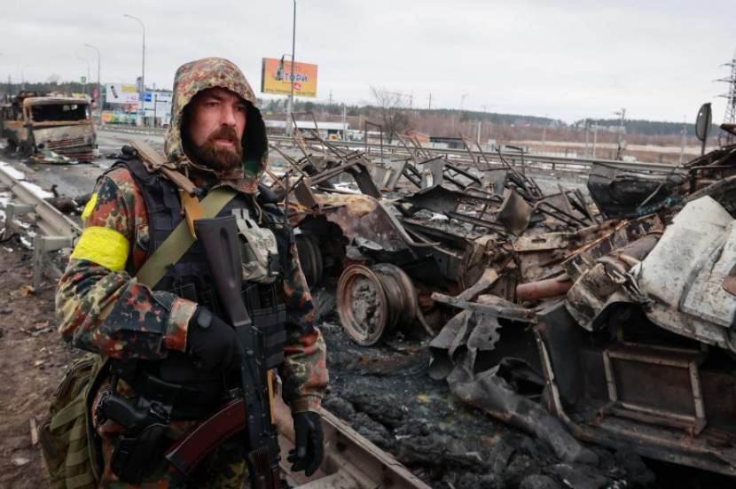 Seorang pria bersenjata berdiri di dekat sisa-sisa kendaraan militer Rusia di Bucha, dekat Kyiv, Selasa, 1 Maret [Serhii Nuzhnenko/AP Photo]