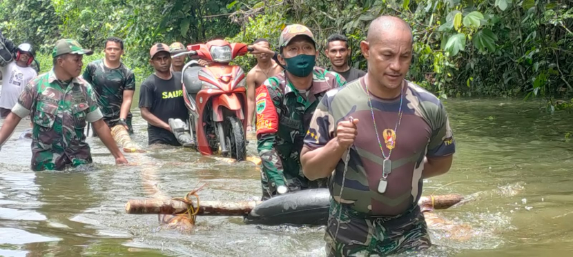 Prajurit Kodim 1803/Fakfak membantu menyeberangkan sepeda motor warga yang terjebak banjir.