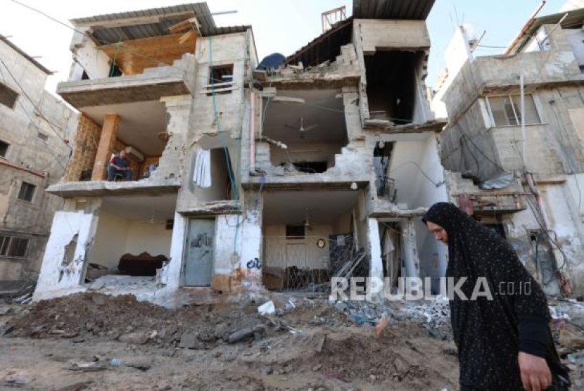 Perempuan Palestina sedang berjalan di sekitar bangunan yang rusak. (EPA-EFE/ALAA BADARNEH)