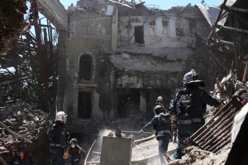 Pegawai Kementerian Situasi Darurat Republik Rakyat Donetsk membersihkan puing-puing di samping gedung teater Mariupol yang rusak selama pertempuran sengit di Ukraina timur [File: AP]