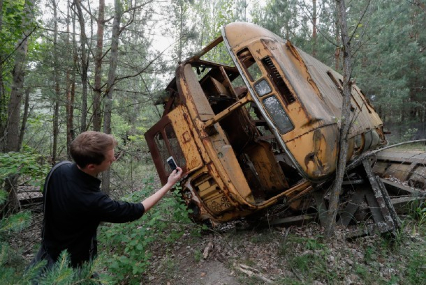 Pengunjung berfoto dekat bus yang ditinggalkan begitu saja setelah insiden nuklir Chernobyl di Rusia. On This Day: 26 April 1986 Tragedi Chernobyl, Lokasi Bisa Dihuni Manusia 3.000 Tahun Lagi. Foto: EPA