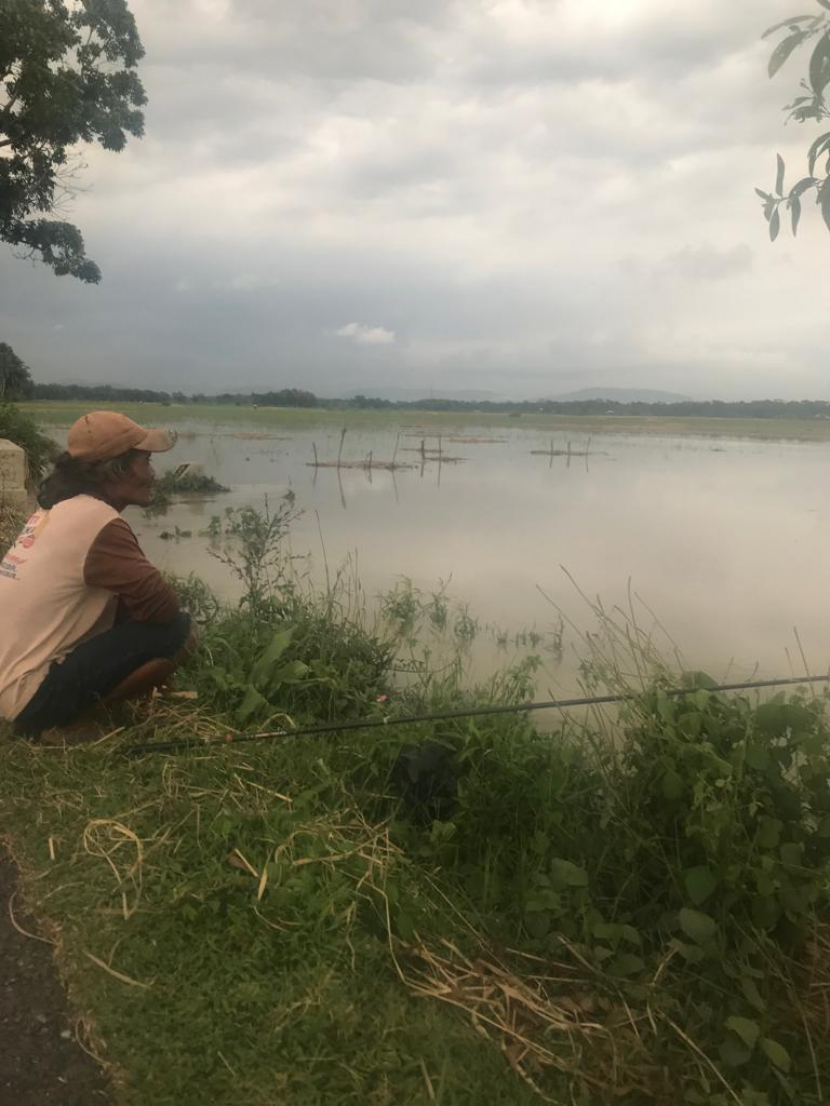 Seorang buruh tani menghibur diri dengan cara memancing pada sebuah lahan sawah milik orang lain yang sedang banjir di masa panen. Banjir meremdam dan merusakkan tananam padi yang sudah siap panen.