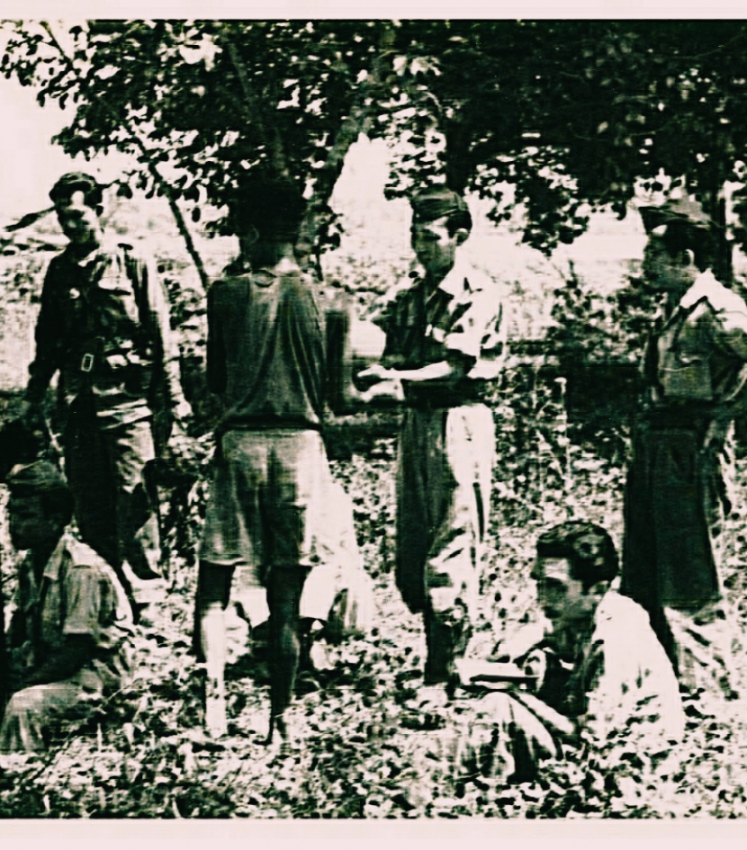 Foto Suasana front Bekasi 1947: Mufreni Mu'min, TKR, berdiri tengah hadap kamera, menerima buah kelapa. Rosihan Anwar, wartawan perang, duduk kanan, membaca catatan. (Ridwan Saidi).