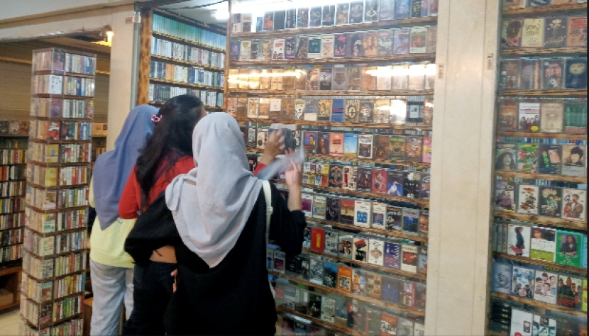 Beberapa remaja sedang memperhatikan berbagai kaset yang dijual di kios kaset di Blok M, Jakarta Selatan. Karena kios sempit, tiga remaja terlihat memperhatikan kaset-kaset di depan pintu kios, Rabu (14/6/2023). Semula, kios jaset itu adalah kios buku lawas.